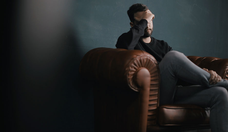 A foto mostra um homem sentado na cadeira com a mão no rosto preocupado com o isolamento social